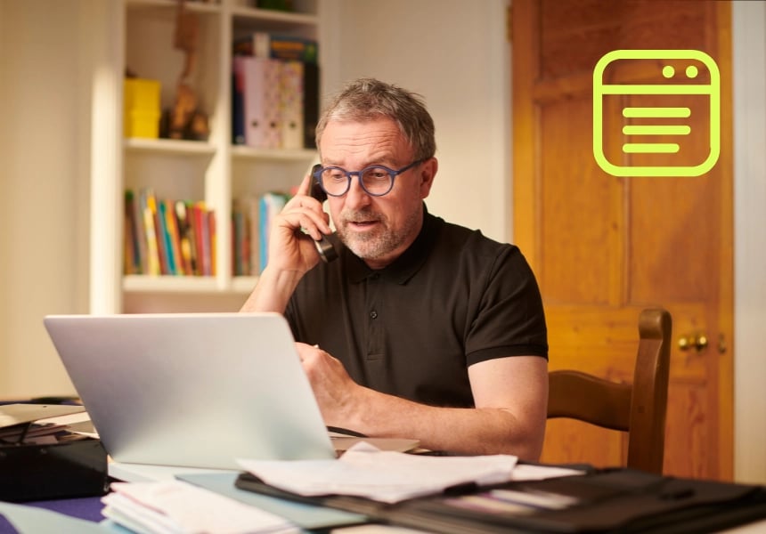 En mand sidder foran sin laptop og taler i telefon.